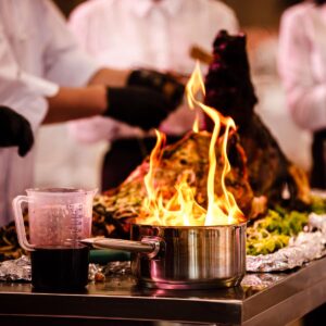 Chef esperto esegue una preparazione flambé durante uno show cooking per eventi